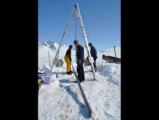 Researchers standing on the frozen lake inspect the coring tube that will be lowered to the lake floor and driven into the sediment below. (Photo courtesy of William D'Andrea)