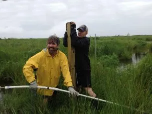 Keith holding the post while Don gets ready to use the pressurized water jet to help insert it into the ground.