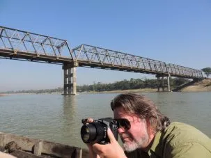 Chris on the boat taking a photo with the highway bridge over the Kushiara River in the background