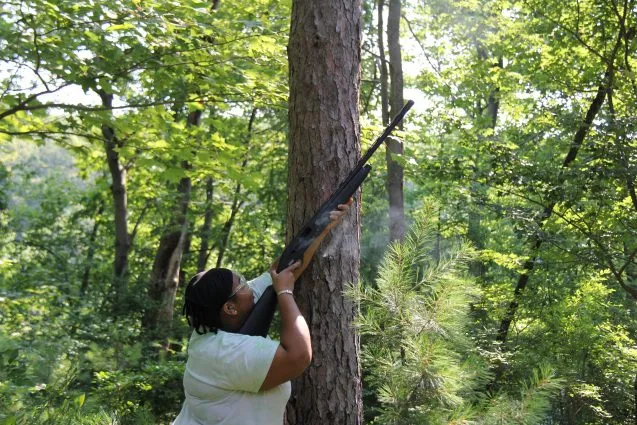 patterson pointing a shotgun up into the tree canopy