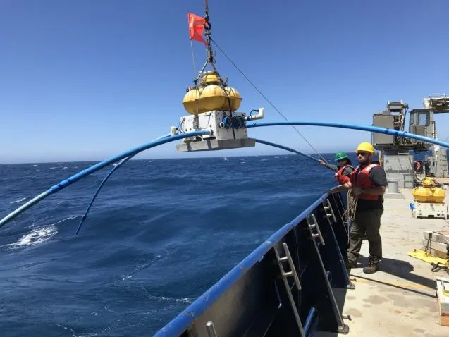 crane lifts a yellow sensor over the side of the ship