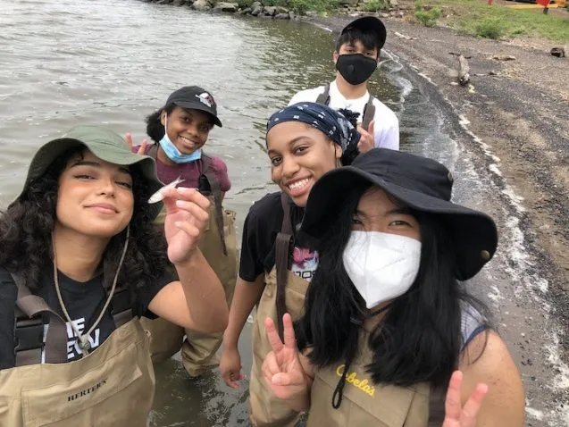 high school students in waders stand in river